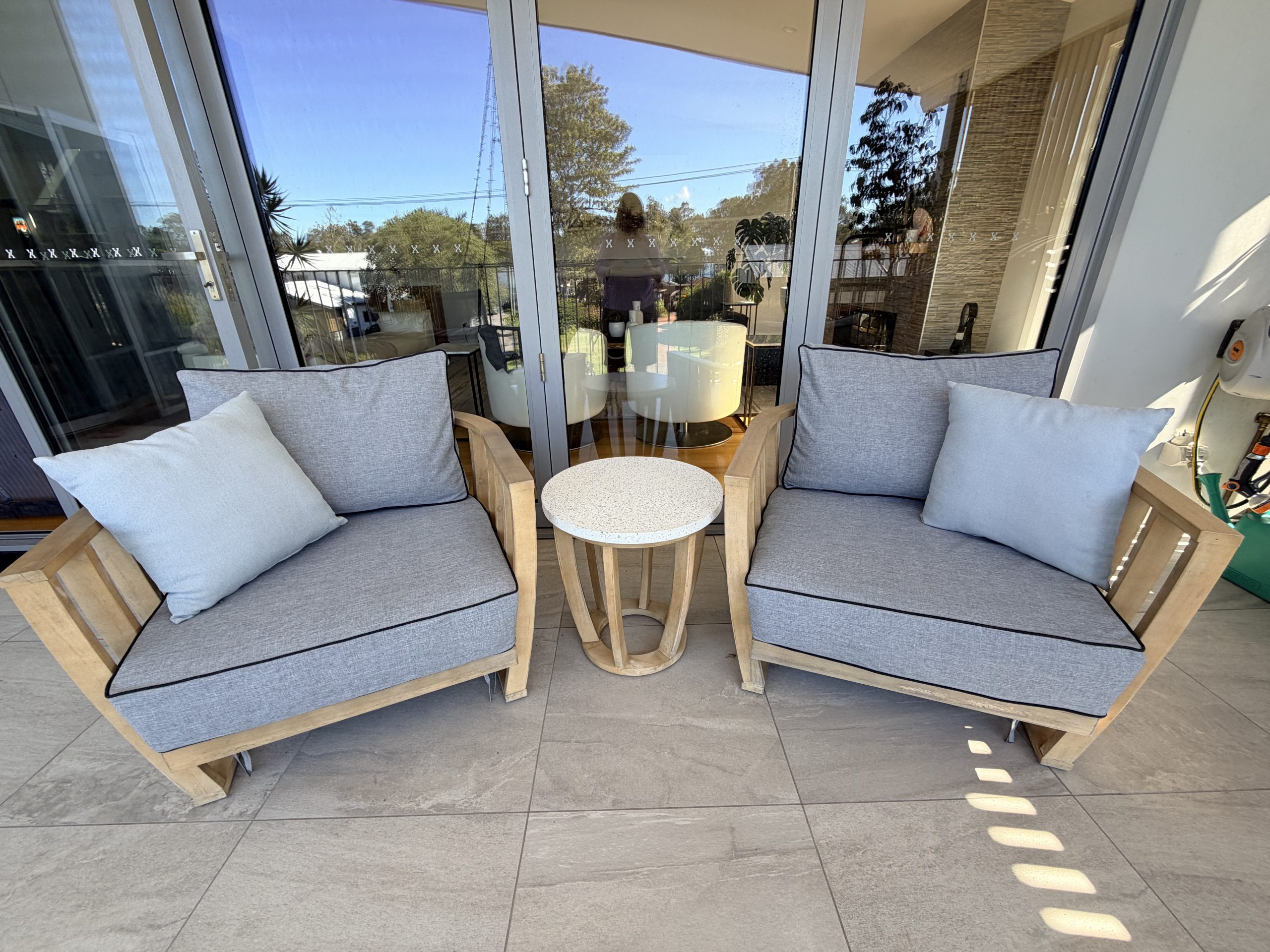 Custom made outdoor lounge cushions in grey with black piping, fitted to a customer’s timber armchairs on their patio in Australia.